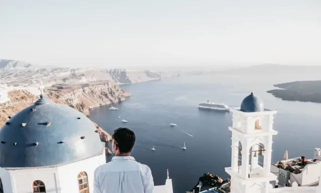 A man gazes at the caldera on a gay Greek island, with iconic blue domes and white architecture overlooking the Aegean Sea.