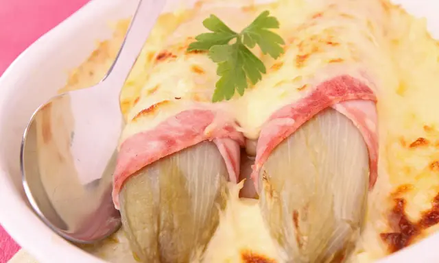 Deux endives braisées enveloppées de jambon, nappées de fromage fondu et gratiné, garnies d'une feuille de persil. Un plat réconfortant.