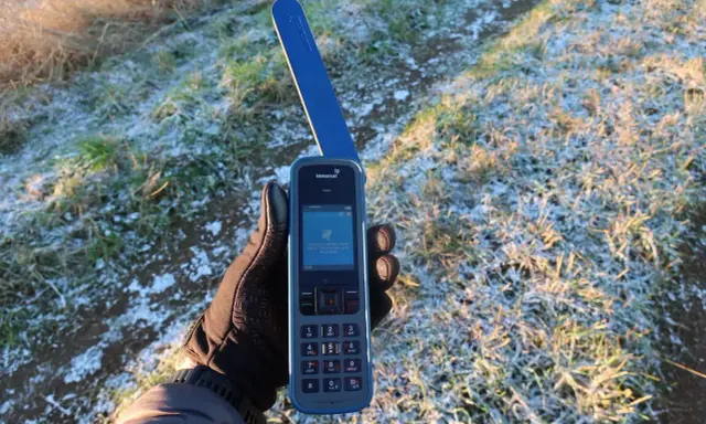 Ręka w rękawiczce trzyma telefon Inmarsat IsatPhone, gotowy do nawiązania połączenia przez telefonię satelitarną w mroźny poranek.
