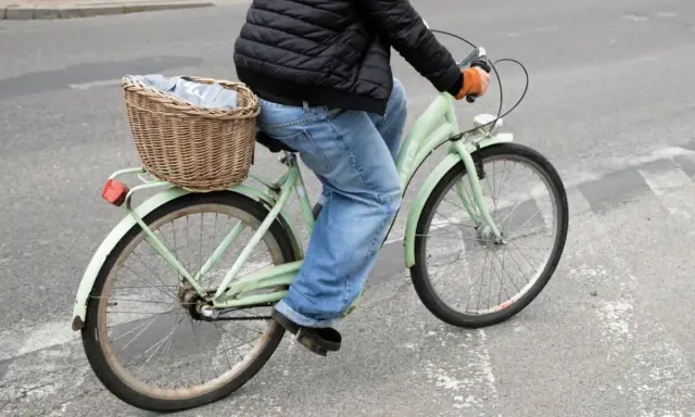 Osoba na rowerze z koszykiem pełnym ubrań wykonuje przejazd rowerem przez pasy.
