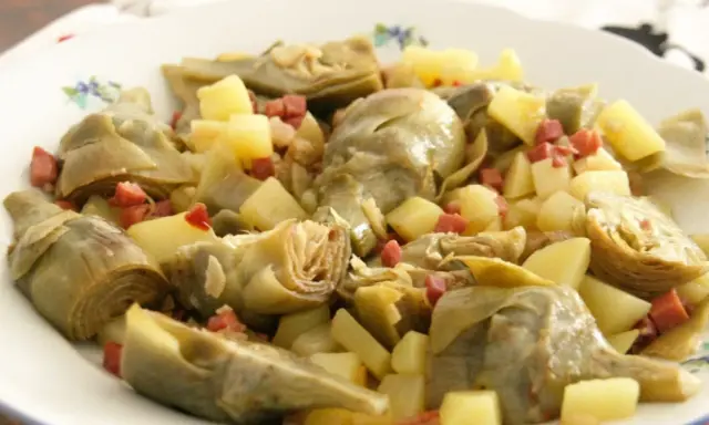Plato de alcachofas tiernas y patatas cortadas en cubos, salpicado con trocitos de jamón. Un manjar casero.