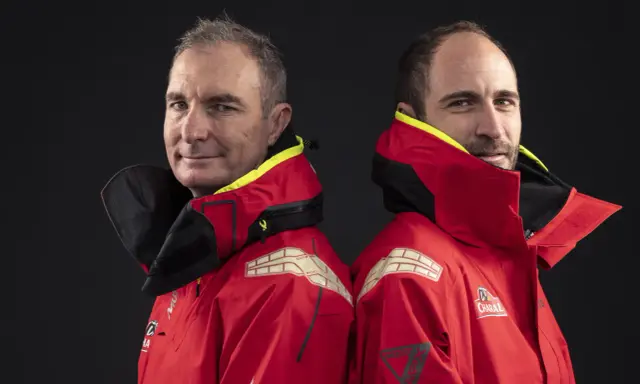 Morgan Lagravière et son coéquipier, deux marins en veste rouge, prêts pour l'aventure en mer.