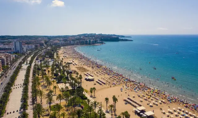 Tłum ludzi cieszy się słońcem na plaży, a w tle widać miasto. To idealne miejsce na wakacje, pełne atrakcji Costa Dorada.
