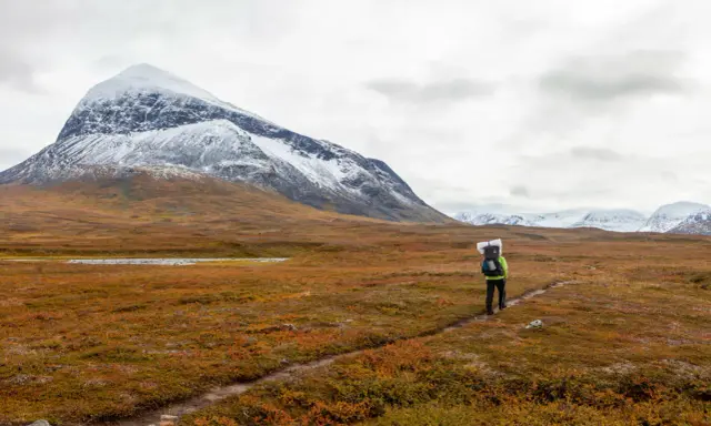 Vandrare på Kungsleden i Sarek med snöklädda berg i bakgrunden och höstens färger i förgrunden.