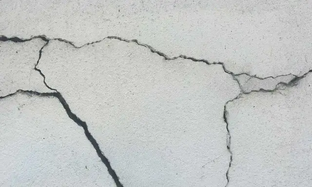 Pęknięcia na jasnej powierzchni betonu, świadczące o procesie karbonatyzacji.