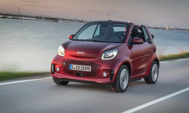 El Smart EQ Fortwo, cual es el coche más pequeño del mercado, se desplaza ágilmente por una carretera costera al atardecer.