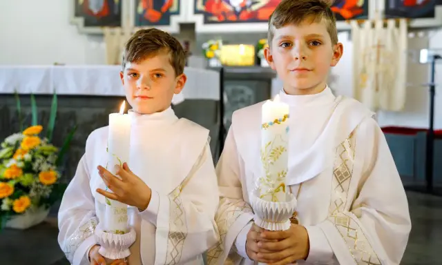 Dwóch chłopców w albach trzyma zapalone świece. Czy do komunii potrzebna jest świeca? Tak, symbolizuje światło Chrystusa.
