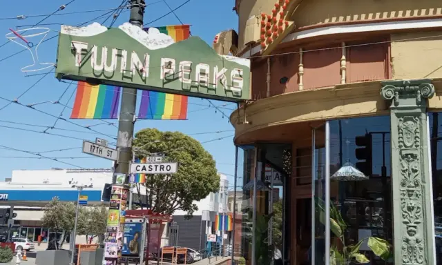 The iconic Twin Peaks sign hangs above Castro Street, a vibrant symbol of the gay area of San Francisco, adorned with rainbow flags.