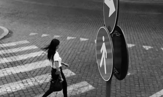 Donna attraversa la strada, un momento catturato con la street photography tecnica. Segnali stradali indicano la direzione.