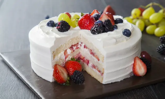 Pyszny tort z bitą śmietaną i mascarpone, przełożony truskawkami i owocami leśnymi. Udekorowany świeżymi owocami.