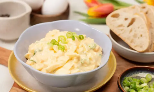Cremiger Eiersalat mit Joghurt und Gurke, garniert mit Frühlingszwiebeln, serviert mit Brot.
