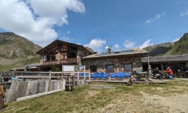 Rifugio Mont Fallère, uno dei rifugi Valle d'Aosta facili, accoglie escursionisti con le sue strutture in pietra e legno, circondato da verdi pendii e montagne.