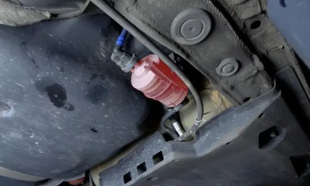 El filtro de combustible, de color rojo y transparente, está ubicado debajo del coche, cerca del tanque.