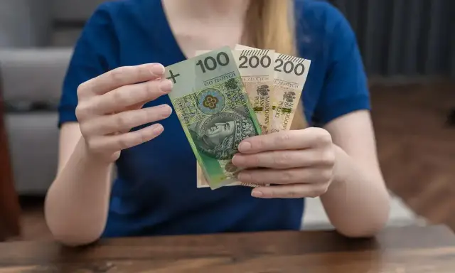 Kobieta trzyma polskie banknoty 100 i 200 zł. Zastanawia się, urlop macierzyński ile płatny.