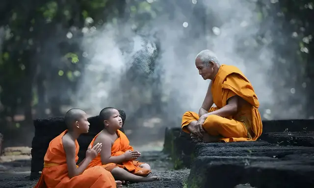 Äldre munk i orange kläder undervisar två unga munkar i en lugn miljö, en scen av buddhistisk puja.