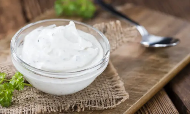 Una ciotola di panna acida cremosa, perfetta per la tua prossima ricetta. Un cucchiaino e un rametto di prezzemolo completano la scena rustica.