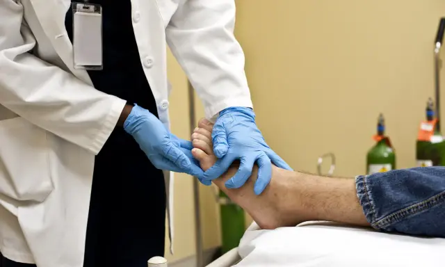 Un professionnel de santé examine un pied, possiblement pour une plaie diabétique, avec des gants bleus. L'application de bétadine est une étape courante pour le soin des plaies.