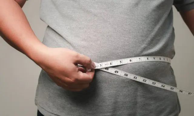 Eine Hand misst mit einem Maßband die Taille. Viele fragen sich, wo nimmt man zuerst ab – oft ist es der Bauch.