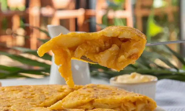 Un tenedor levanta un trozo jugoso de tortilla de espaguetis, mostrando su interior dorado y tierno.