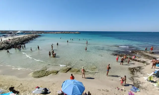 Gente in spiaggia e in mare vicino alla torre vado lungomare. Acqua cristallina e cielo azzurro.
