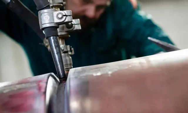 Saldatore esperto esegue saldatura ad arco sommerso su un tubo metallico, creando un giunto robusto.