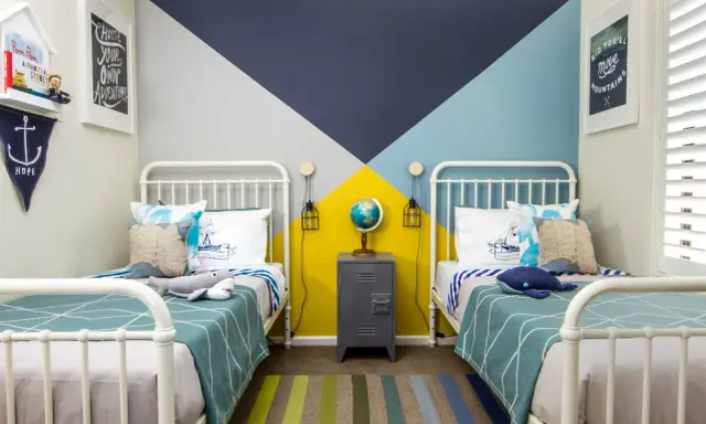 Habitaciones juveniles con camas blancas y pared geométrica en azul, gris y amarillo. Alfombra de rayas y decoración náutica.