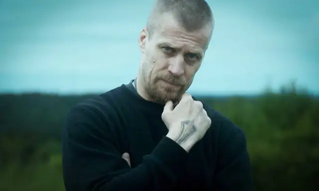 Jens Hultén, känd från filmer och tv-program, med en intensiv blick och en tatuering på handen.