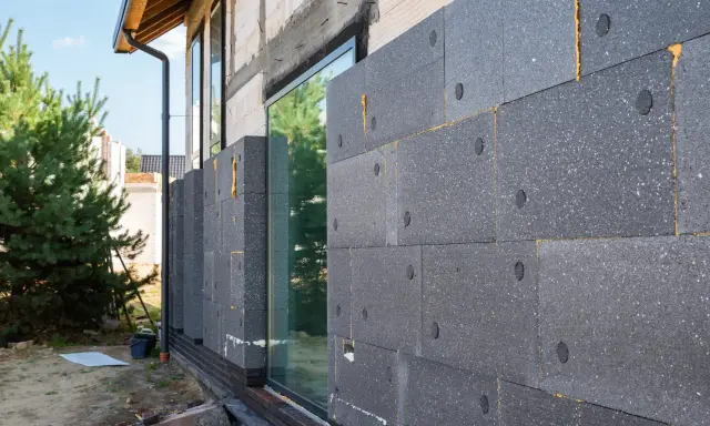 Graue Dämmplatten werden an der Hauswand angebracht, um das Haus zu isolieren.