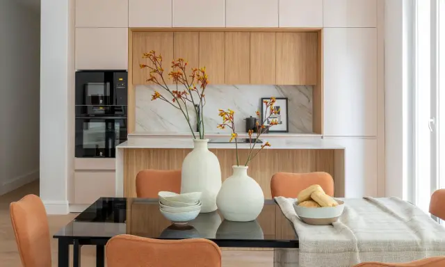 Dos jarrones blancos con flores anaranjadas y amarillas, cuencos apilados y un bol con panecillos son elementos decorativos que poner encima de una mesa de comedor.