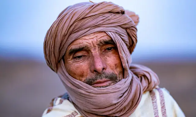 Porträt eines alten Berber Hirtennomaden mit einem Turban und traditioneller Kleidung, dessen Gesicht von der Sonne gezeichnet ist.