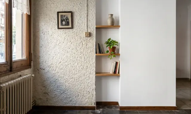 Un rincón con un radiador antiguo, un cuadro familiar y estanterías. La textura de la pared es rugosa, pero merece la pena quitar el gotelé para un acabado más liso.