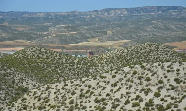 Paisaje árido del desierto de Monegros con colinas cubiertas de matorral y una torre de iglesia solitaria al fondo.