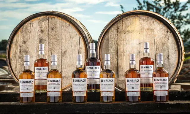 Butelki whisky BenRiach stoją przed beczkami, które zdradzają, skąd pochodzi whisky.