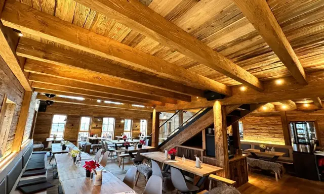Gemütliches Holzinterieur eines Restaurants mit Holzbalken und Tischen.