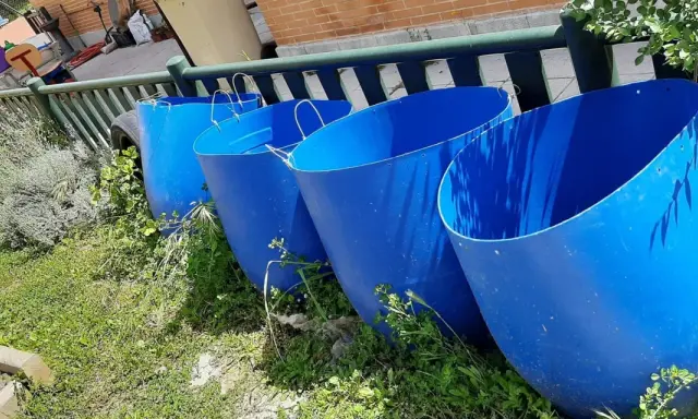 Cuatro grandes barriles azules listos para recoger agua de lluvia en el campo.