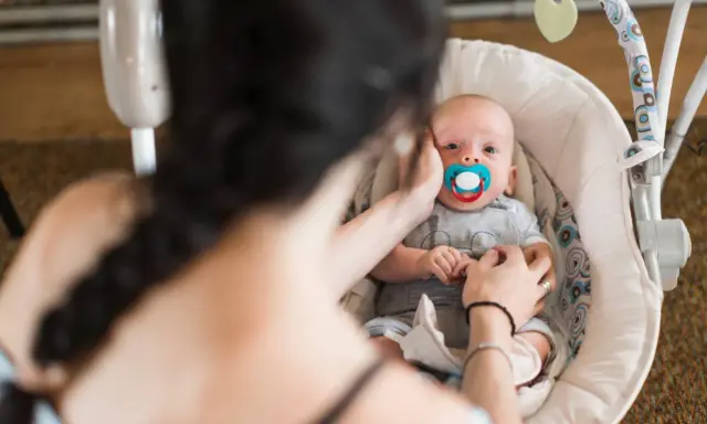 Maluszek w bujaczku polecanym przez fizjoterapeutów. Mama delikatnie głaszcze go po główce, uspokajając.