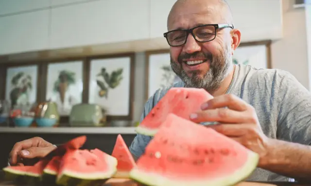 Glücklicher Mann mit Brille isst Wassermelone. Die Wassermelone Nachteile sind, dass sie schnell aufgebraucht ist.