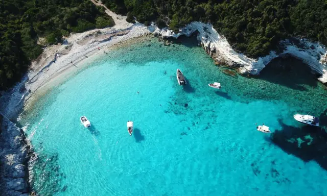 Idealne wakacje na Paxos: turkusowa woda, białe skały i łodzie unoszące się na falach.