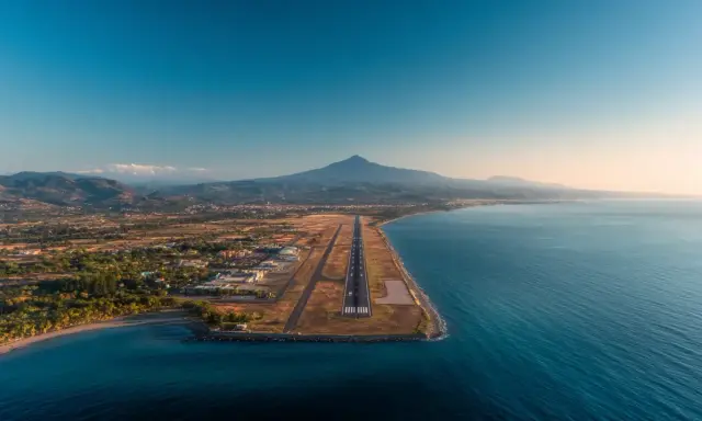 Flygplats vid havet med berg i bakgrunden. En landningsbana sträcker sig ut mot vattnet, en vy som påminner om Palermo flygplats.