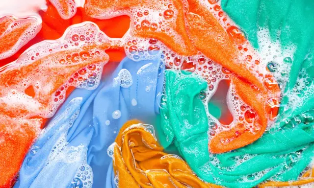 Ropa de color lavadora con burbujas de jabón. Prendas naranjas, azules, verdes y amarillas sumergidas en agua.
