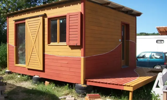Maisonnette en bois aux couleurs vives, rappelant un nuancier peinture suédois. Porte coulissante jaune, volets rouges.