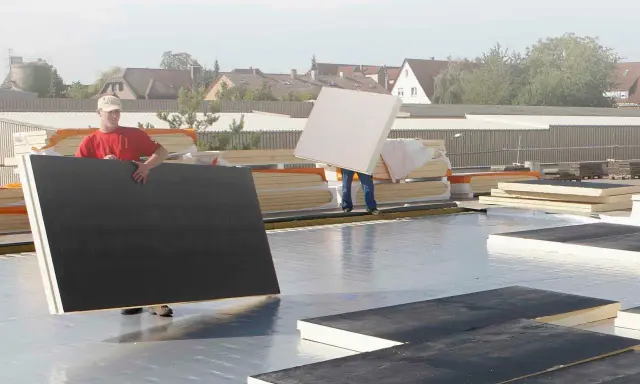 Arbeiter verlegen Dämmplatten auf einem Dach. Die Platten entsprechen der DIN 18234 und werden für die Dachisolierung verwendet.