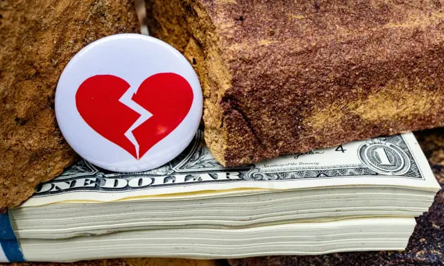 Symbol złamanego serca na stosie dolarów, między kamieniami. Nieoficjalna separacja, gdzie pieniądze dzielą.