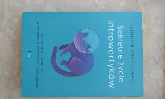Książka "Sekretne życie introwertyków" z kotem w hełmie kosmicznym. Przewodnik dla cichych i tych, którzy chcą ich zrozumieć.