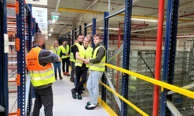 Grupa osób w kamizelkach odblaskowych zwiedza magazyn CEVA Logistics. To potencjalna ceva logistics praca.