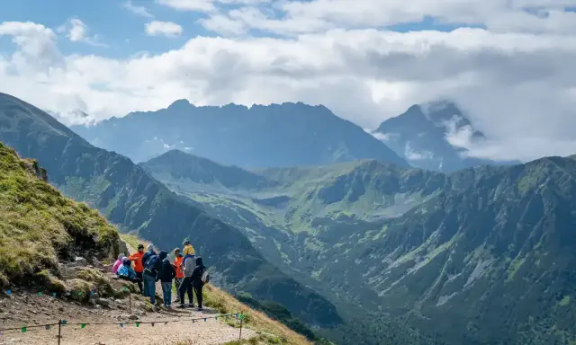 Grupa turystów odpoczywa na szlaku z widokiem na majestatyczne Tatry. W oddali majaczy Kasprowy Wierch, otoczony chmurami.