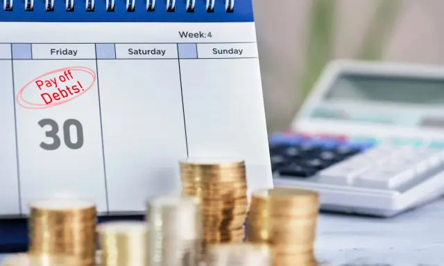 Kalendarz z zaznaczonym "Pay off Debts!" i sterty monet. Długi w ZUS to jak więzienie, ale spłata to wolność.