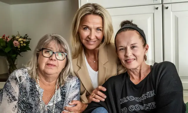 Tre kvinnor, möjligen lill babs barn, ler mot kameran. En kvinna i mitten bär en beige kavaj, den vänstra har glasögon och den högra en svart tröja.