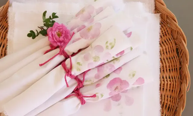 Vita tygservetter med rosa blommor, bundna med rosa snöre och dekorerade med en ros. Vackert dukat för en sommarfest.