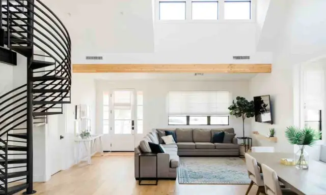Ampio soggiorno con scala a chiocciola nera, divano angolare grigio e trave in legno a vista. Loft idee originali per un ambiente moderno.